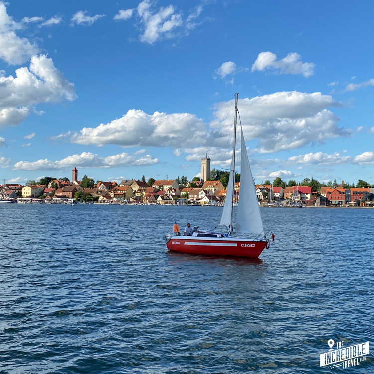 Im Hintergrund die Stadt Mikołajki, im Vordergrund auf dem See ein rotes Segelboot