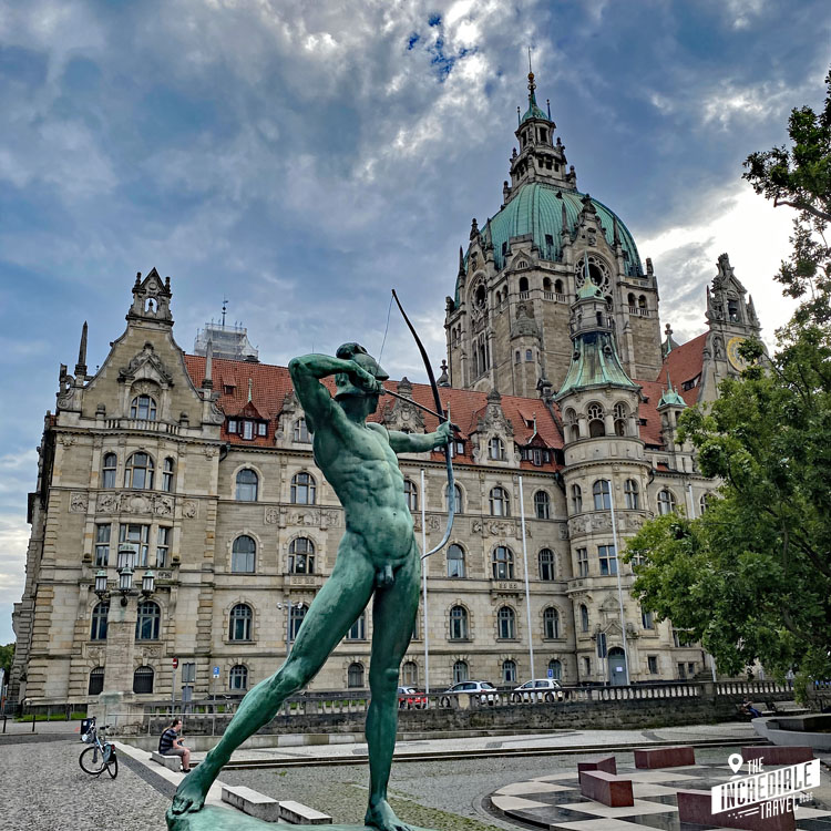 Blick auf die Statue eines nackten Bogenschützen im Vordergrund und das reich verzierte Rathaus im Hintergrund