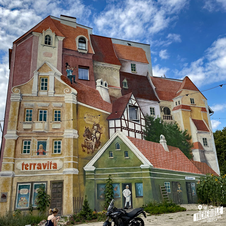 Großes Gemälde an einer Häuserwand: Verschiedene Häuser und ihre Bewohner in 3-D-Optik