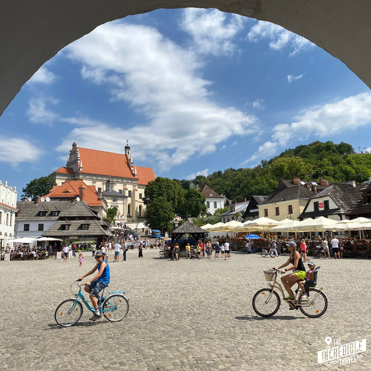 Blick auf den Marktplatz von Kazimierz mit der Kirche auf einer Anhöhe und zwei Radfahrern im Vordergrund