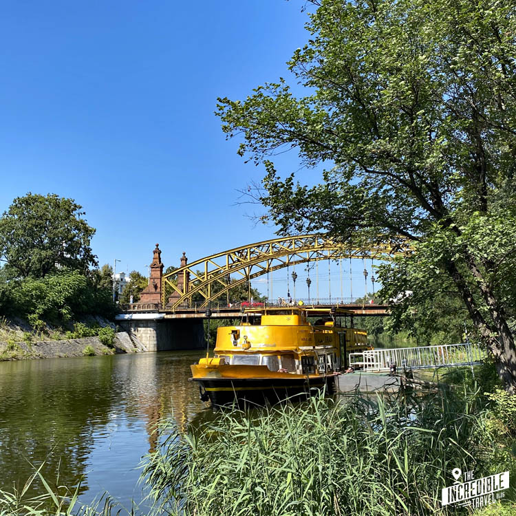 Blick auf eine Bogenbrücke, im Vordergrund ein gelbes Ausflugsboot