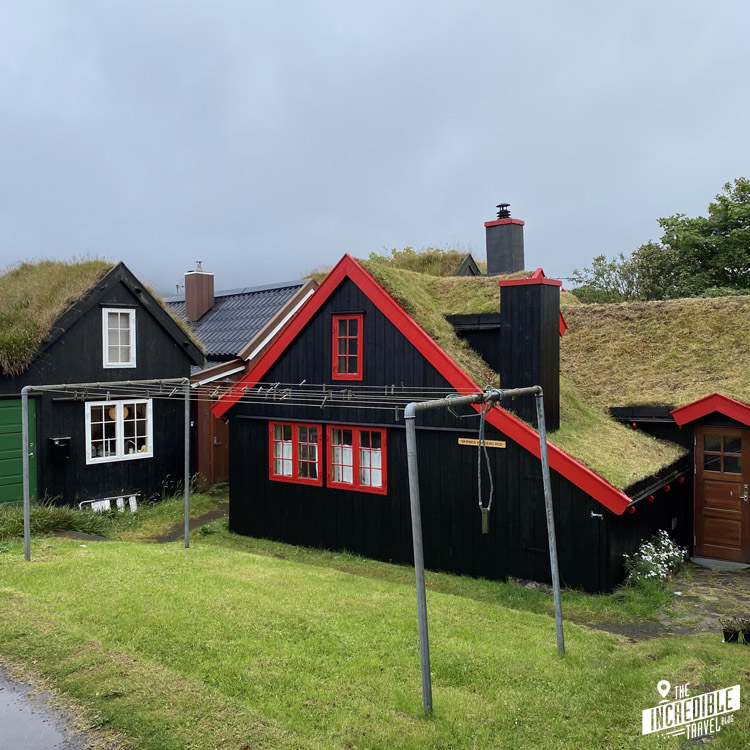 Schwarze Holzhäuser mit Grasdächern und in einem Fall roten Fenstern