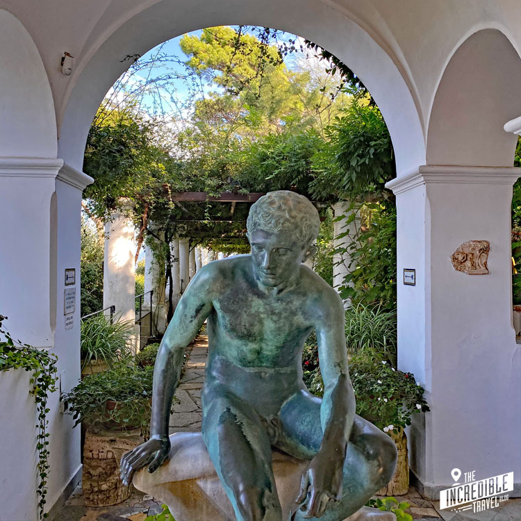 Bronzestatue eines sitzenden Mannes, dahinter Blick durch einen Bogengang in den Garten