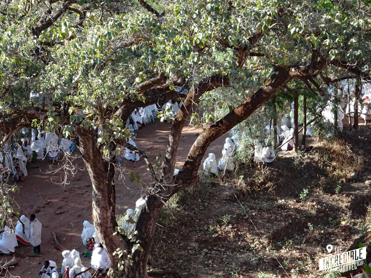 Gläubige warten in weißen Gewändern im Schatten der Bäume an den Felsenkirchen in Lalibela