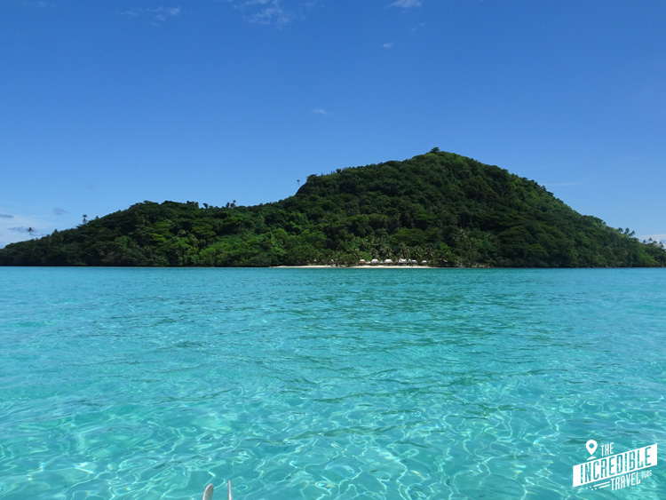 Aquamarinblaues Wasser, im Hintergrund eine felsige Insel mit Sandstrand