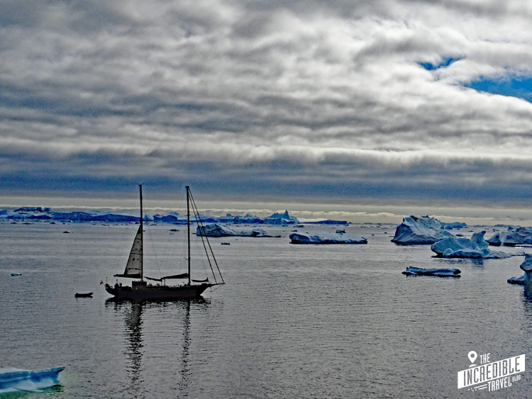 Segelboot angeht in der Bucht, umgeben von einzelnen kleinen Eisbergen