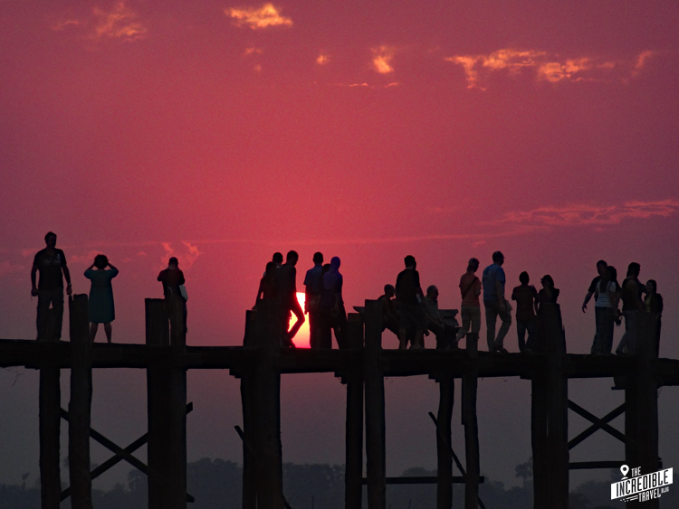 Holzbrücke im Sonnenuntergang mit Menschen, von denen nur Silhouetten zu sehen sind