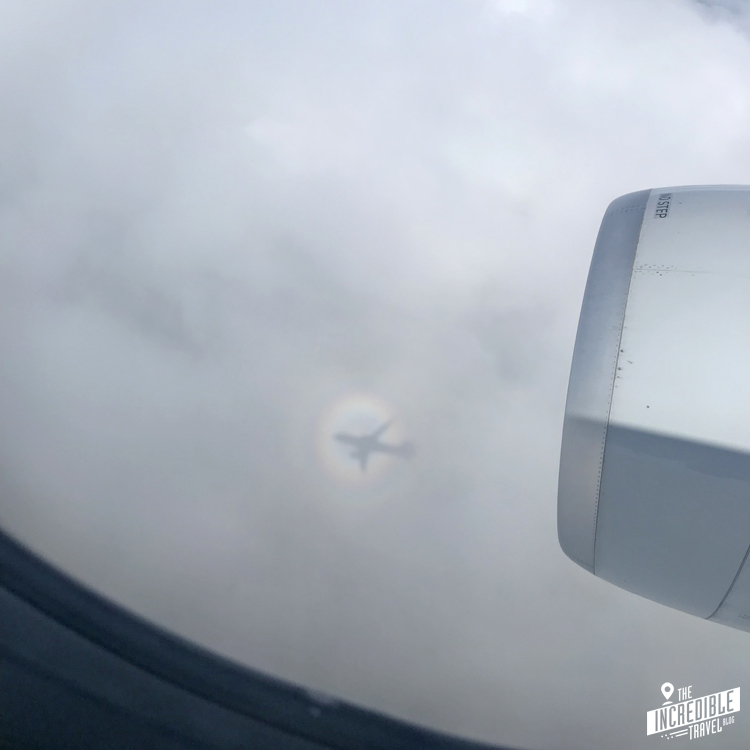 Blick aus dem Flugzeugfenster auf den Schatten des Flugzeuges auf der Wolkendecke