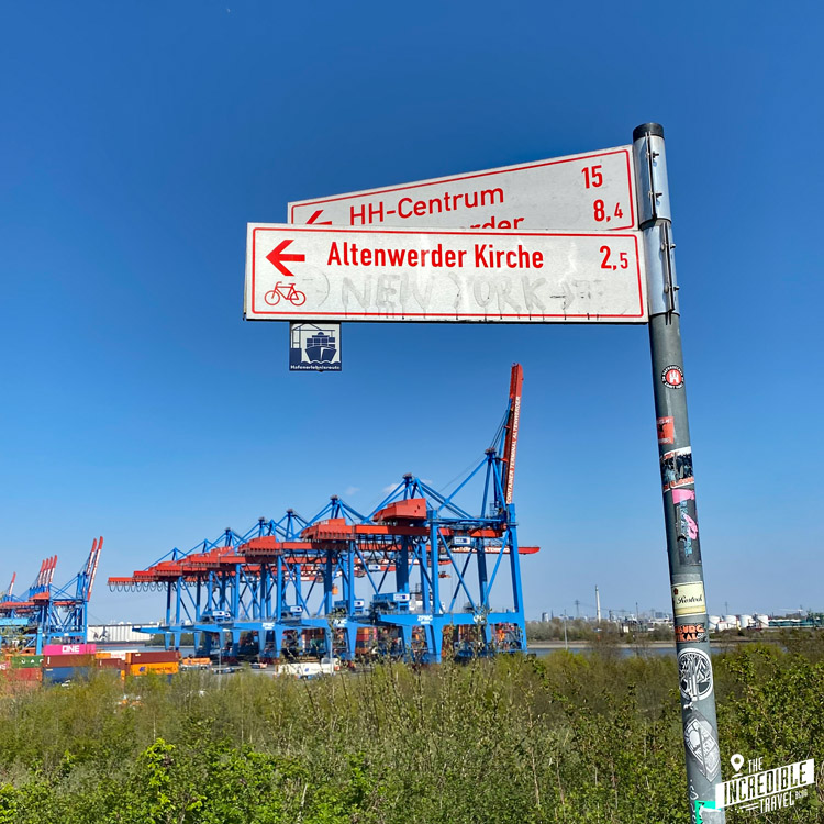Hinweisschilder für Radwege, im Hintergrund das Container-Terminal Altenwerder