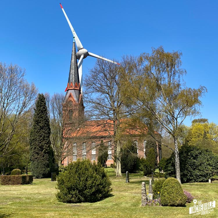 Blick auf Kirche, Kirchhof und eine Windkraftanlage
