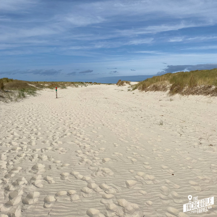 Breiter Sandweg mit zahlreichen Fußspuren und Dünen an beiden Seiten