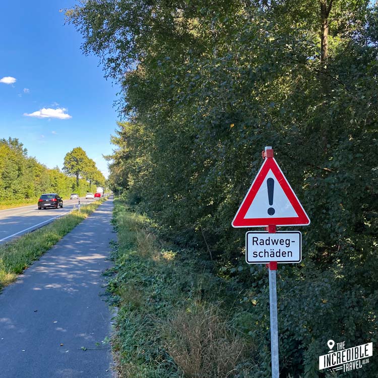 Relativ schmaler Radweg an einer Bundesstraße mit dem Hinweisschild "Radwegschäden"