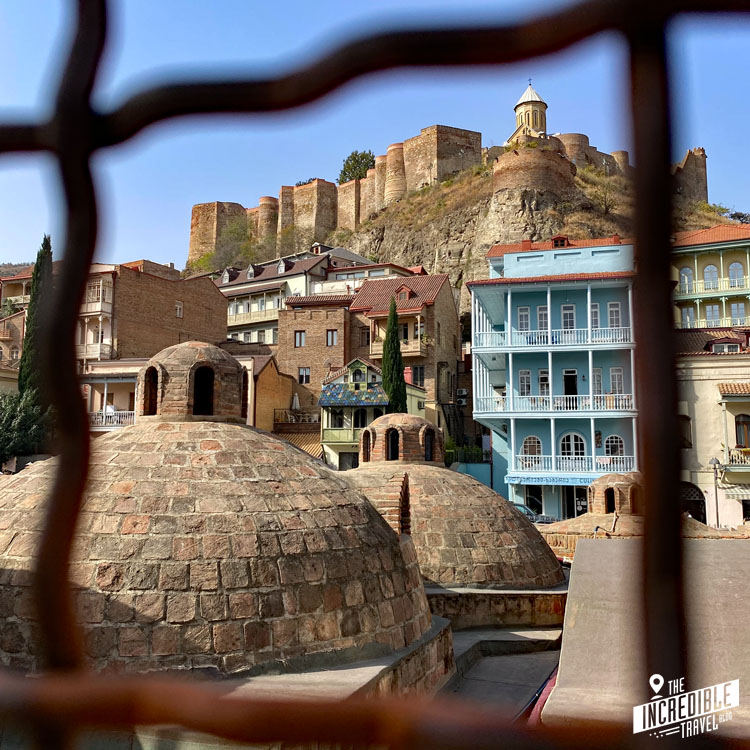Blick durch ein Gitter auf Häuser der Altstadt und die Festung auf einem Berg