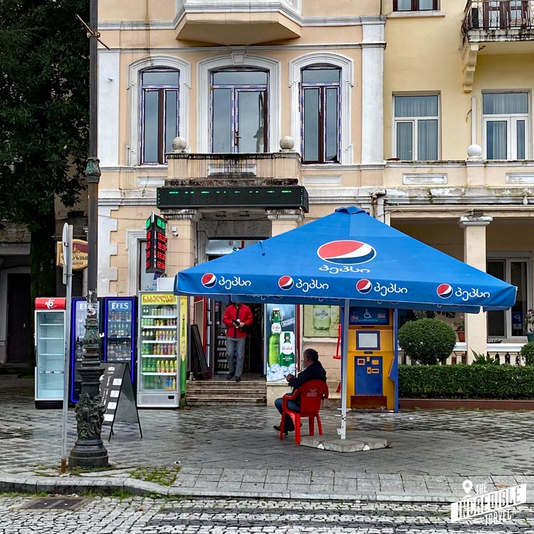 Frau sitzt unter Pepsi-Sonnenschirm vor einem Kiosk