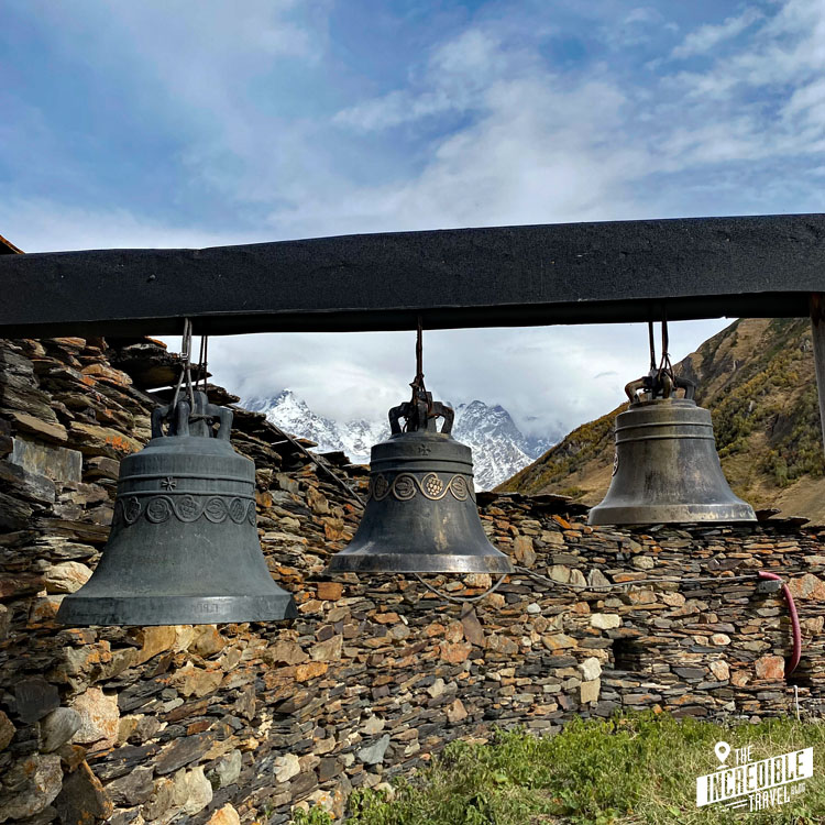 Drei Glocken an einem Balken vor Bergpanorama