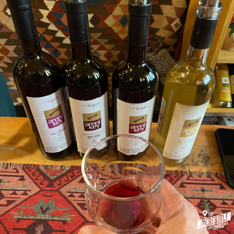 vier Weinflaschen, dafür ein Glas Rotwein von einer Hand gehalten