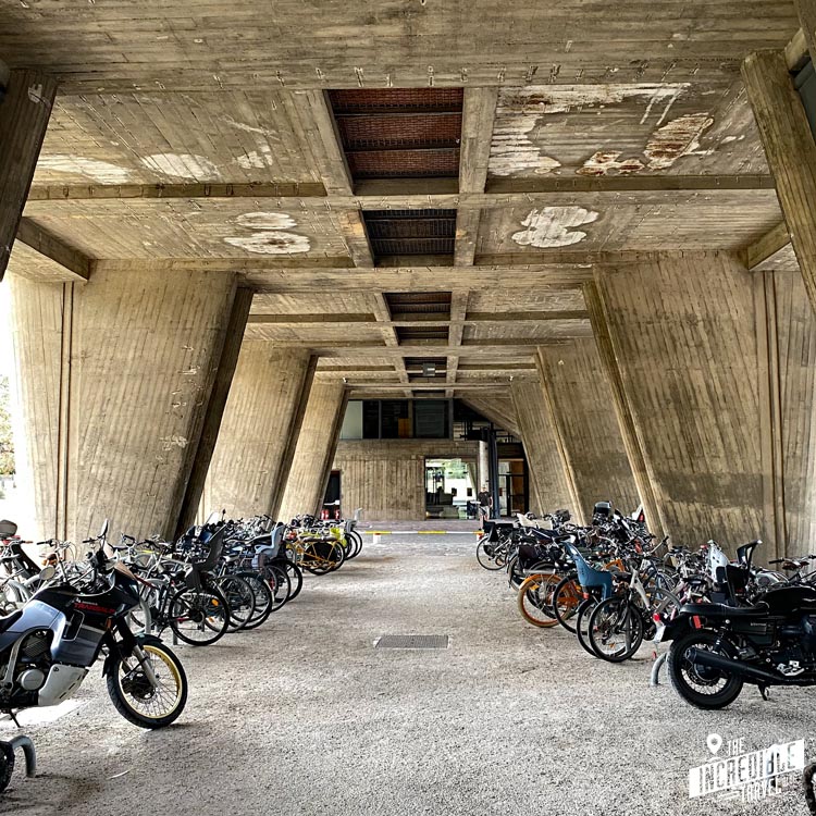 Blick auf Motorräder und Fahrräder neben den großen Betonstützen des Gebäudes