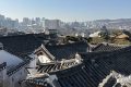Dächern traditioneller koreanischer Häuser im Vordergrund, moderne Stadtskyline mit Hochhäusern im Hintergrund.