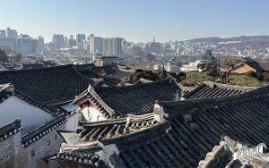 Dächern traditioneller koreanischer Häuser im Vordergrund, moderne Stadtskyline mit Hochhäusern im Hintergrund.
