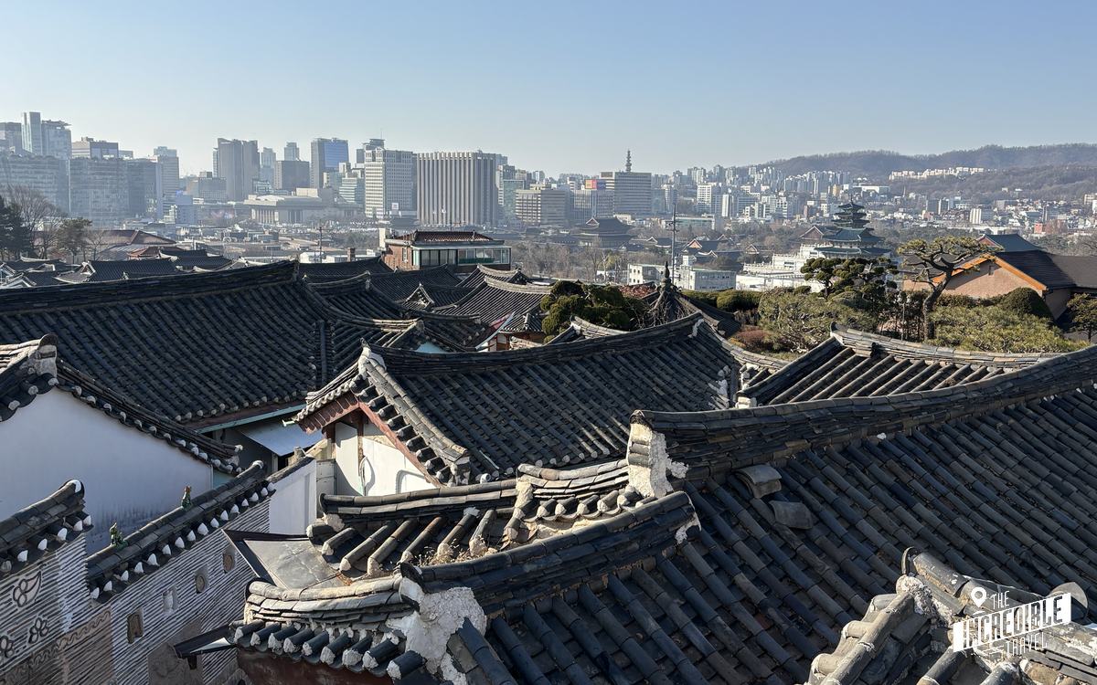 Dächern traditioneller koreanischer Häuser im Vordergrund, moderne Stadtskyline mit Hochhäusern im Hintergrund.