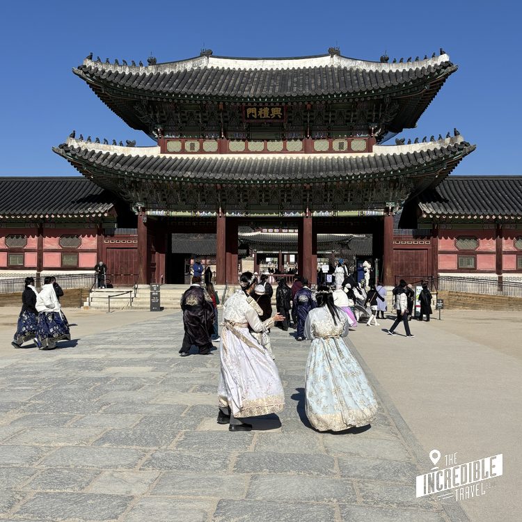 Traditionelles asiatisches Tempelgebäude mit geschwungenen Dächern, Besuchende in historischen Gewändern auf dem Platz vor dem Eingang.