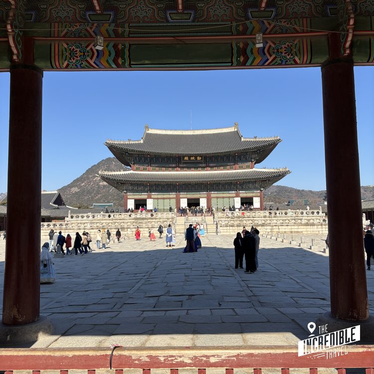 Blick durch ein verziertes Tor auf ein asiatisches Palastgebäude mit geschwungenen Dächern und Besucher auf dem Platz.