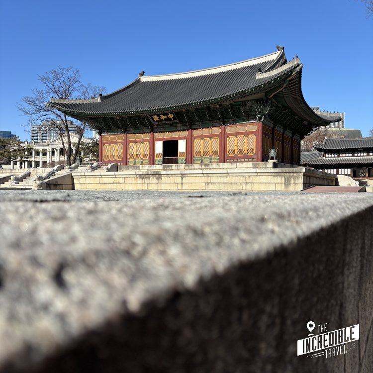 Traditionelles ostasiatisches Tempelgebäude mit roten Türen, geschwungener Dachkante und Steinmauer im Vordergrund.