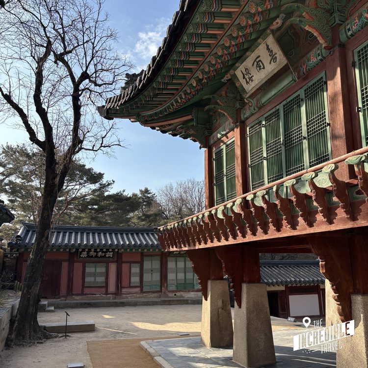 Traditionelles asiatisches Gebäude mit rotem Holzrahmen, grünen Türen und verziertem Dach in einem ruhigen Innenhof mit kahlem