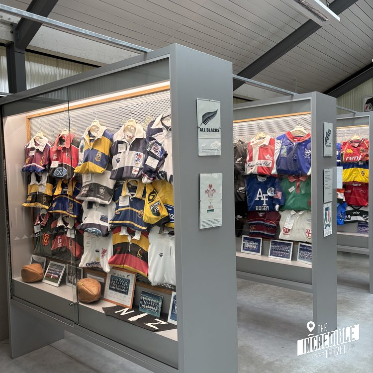 Museumsausstellung mit historischen Rugby-Trikots und -Ausrüstung in beleuchteten Vitrinen unter Industriedach