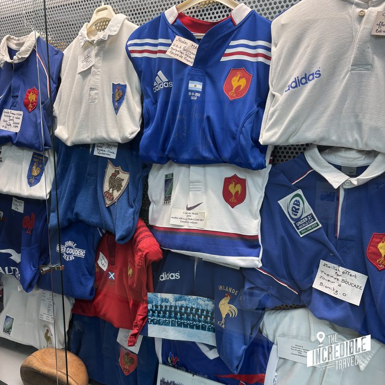 Sammlung historischer Rugbyjerseys in Blau und Weiß mit Wappenschildern hängen auf einem Ständer in einem Museum