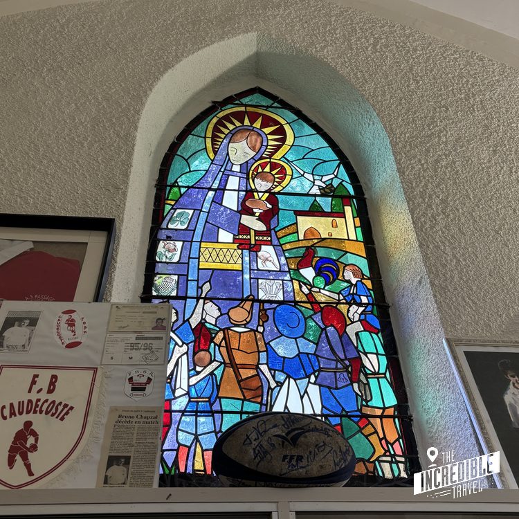 Buntes Kirchenfenster aus Bleiglas mit religiösen Motiven und Heiligenschein in einer weißen Bogennische an der Wand.
