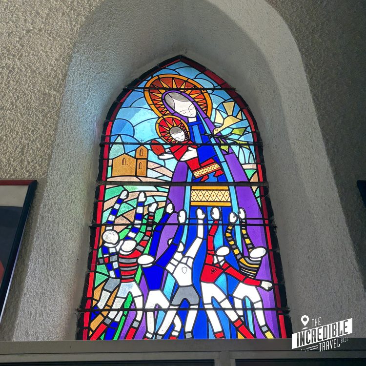 Buntes Buntglasfenster in einer Kirche mit in Blau, Rot, Grün und Gelb. Jungfrau Maria, Jesus und Rugbyspieler.