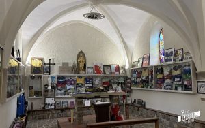 Kapellenraum mit Gewölbedecke, Ausstellungsvitrinen mit Trikots, Fotos und Memorabilien an den Wänden, religiöse Symbole und goldene Statue in der Mitte.