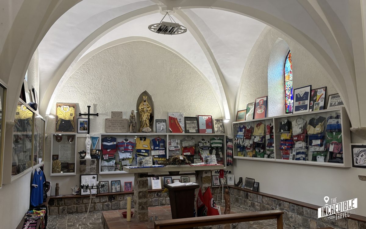 Kapellenraum mit Gewölbedecke, Ausstellungsvitrinen mit Trikots, Fotos und Memorabilien an den Wänden, religiöse Symbole und goldene Statue in der Mitte.