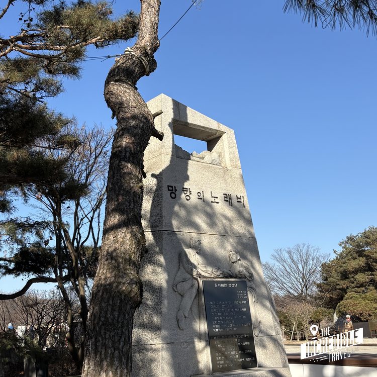 Gedenkstein mit koreanischer Schrift neben einem alten Baum unter blauem Himmel