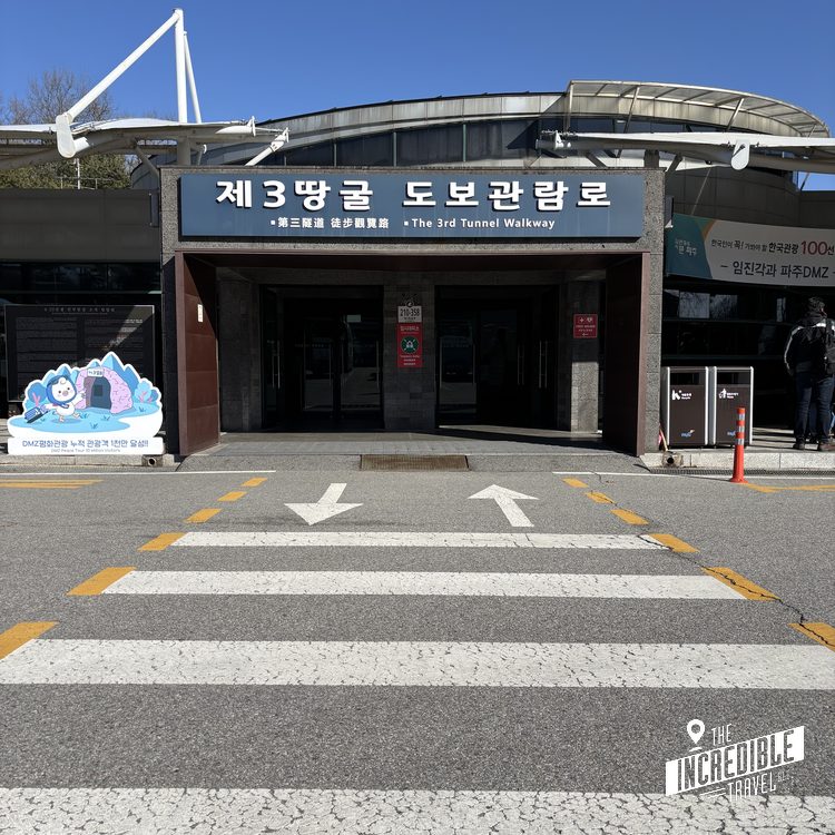 Eingang zum nordkoreanischen Infiltrations-Tunnel mit Zebrastreifen und moderner Architektur unter blauem Himmel.