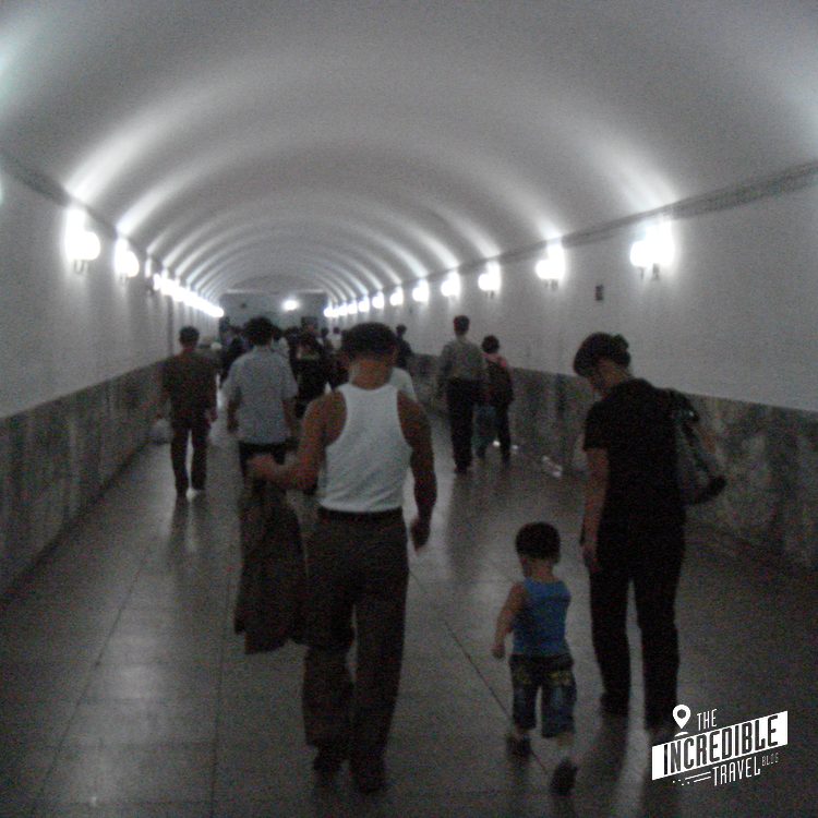 Mehrere Menschen gehen durch einen modern beleuchteten unterirdischen Tunnel mit gewölbter Decke.