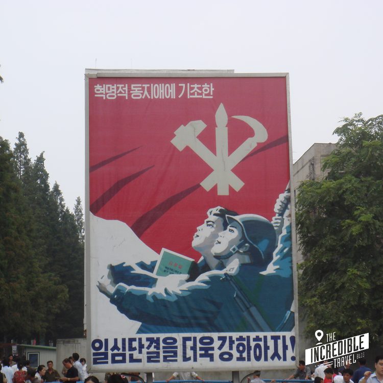 Propagandaplakat mit rotem Hintergrund, weißem Symbol und zwei Personen, die nach oben schauen, koreanischer Text.