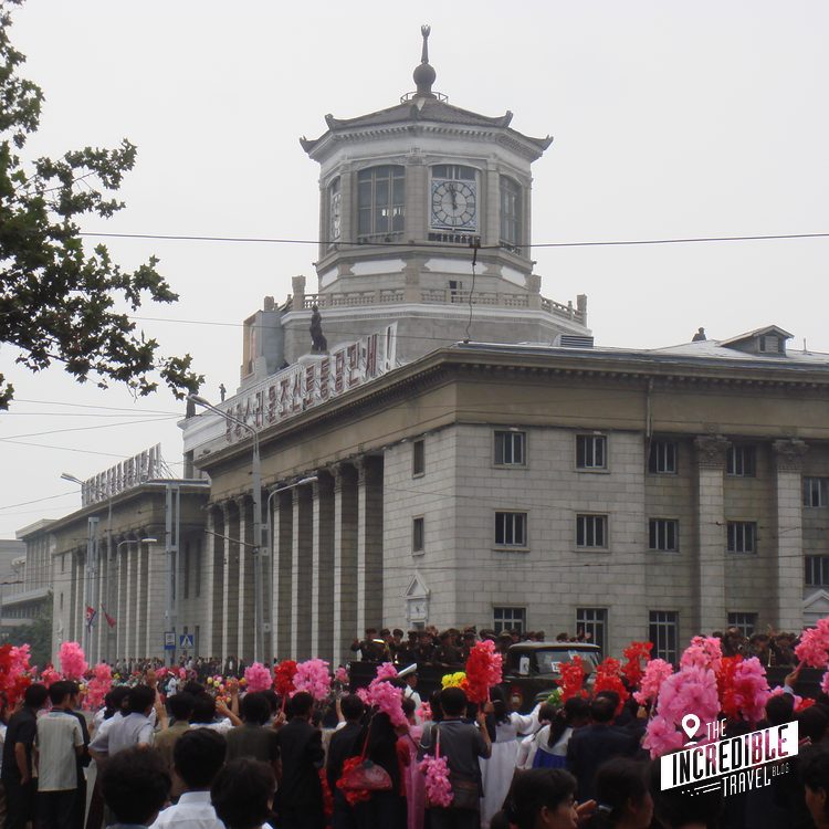 Historisches Gebäude mit Uhrturm und aufragender Spitze, umgeben von Menschenmenge mit pinken Pompons bei Feierlichkeit.