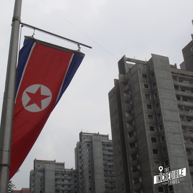 Flagge mit rotem Feld, blauem Rand und weißem Stern an Laternenmast vor Hochhäusern