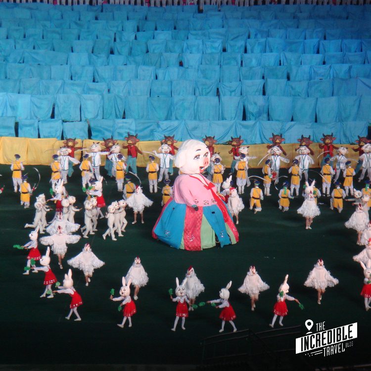 Großes bunte Fest mit Kinderchor in Stadion, blaue Zuschauerplätze und Riesen-Puppe in Karnevalskostüm.