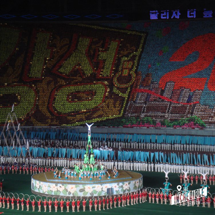 Große Massenveranstaltung mit Tänzern in Rot und Blau, beeindruckende Mosaikkulisse im Hintergrund.