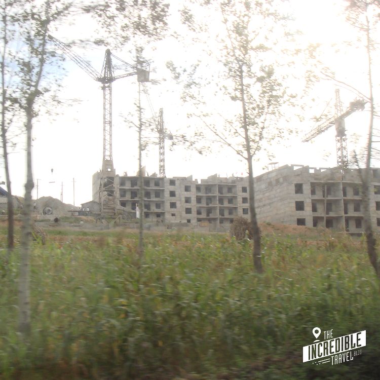 Unvollendete Betongebäude im Rohbau zwischen Bäumen und Feldern mit Strommasten, verschwommene Aufnahme