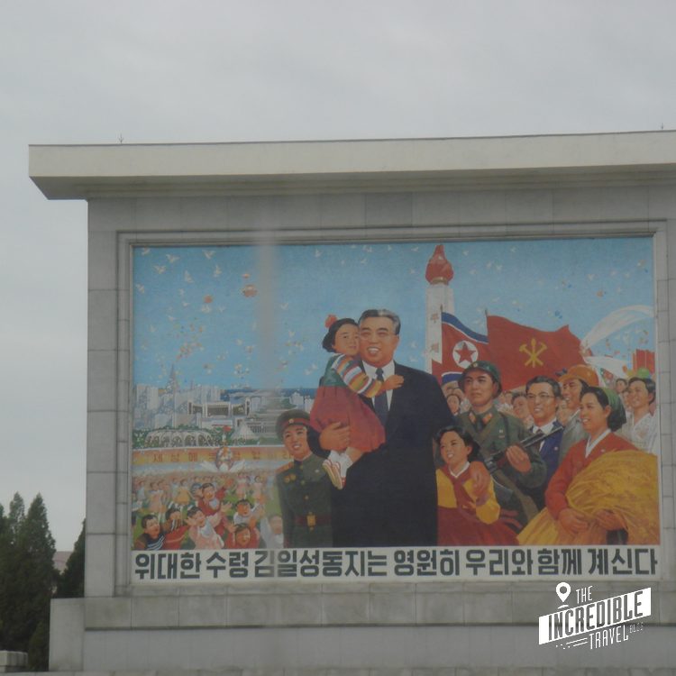 Propagandamural auf grauer Betonwand mit Koreanern, Flaggen und Schriftzeichen in Rot- und Blautönen